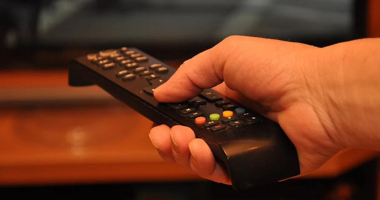 Mão segurando um controle remoto de televisão, ilustrando como cancelar o Globoplay